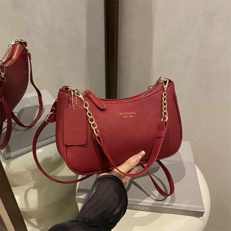 Red pebbled shoulder crossbody bag with gold chain handles and rectangular side charm