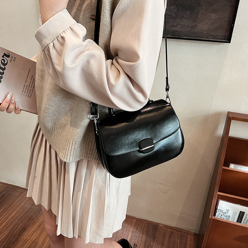 Black crossbody handbag with flap front, gold-tone buckle, and adjustable shoulder strap