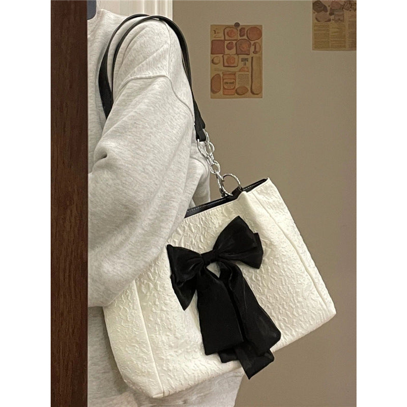 White canvas shoulder tote with black bow charm and silver chain strap