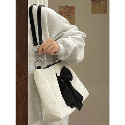 White canvas tote held by hand, black bow detail, silver chain shoulder straps