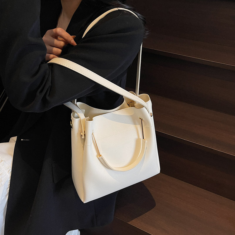 Cream bucket bag with top handles and long crossbody strap, side pocket detail