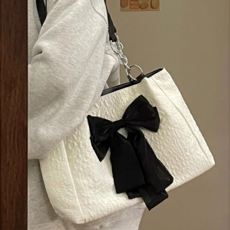 White canvas tote bag with black bow detail and chain shoulder straps