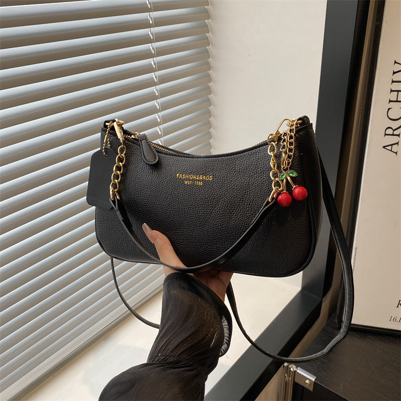 Black pebbled shoulder crossbody bag with gold chain strap and red cherry keychain charm