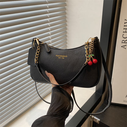 Black pebbled shoulder crossbody bag with gold chain strap and red cherry keychain charm