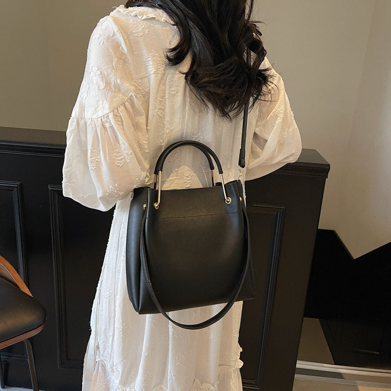 Dark green bucket bag with top handle and crossbody strap worn with white dress