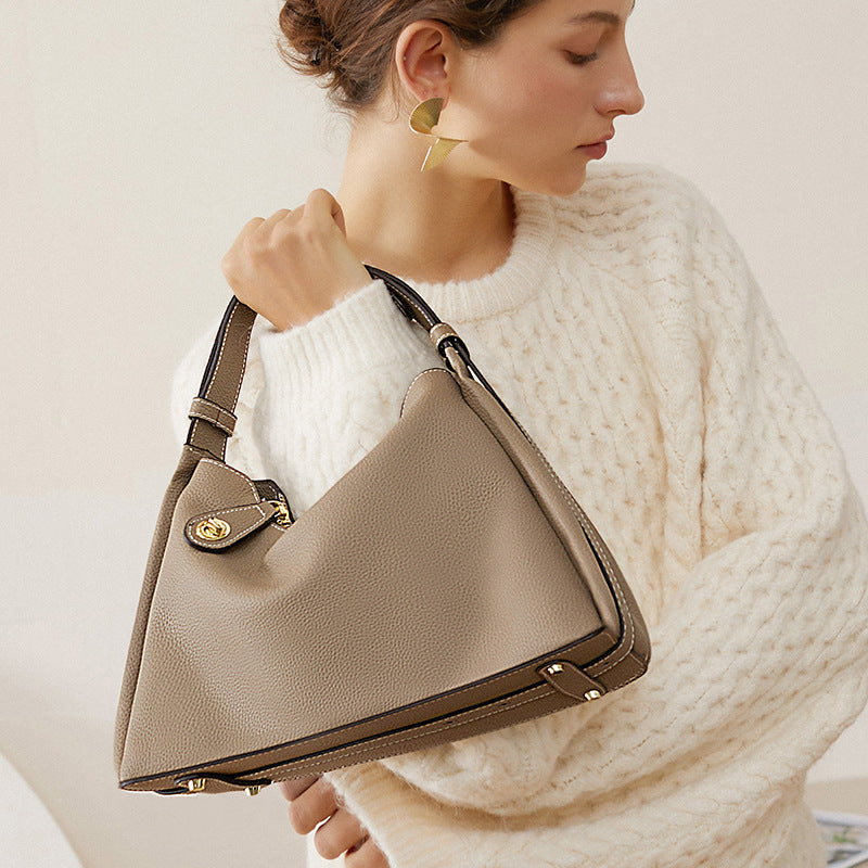 Beige crossbody hobo bag worn on shoulder with gold clasp flap pocket
