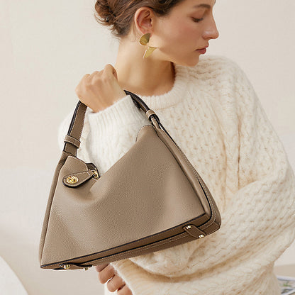 Beige crossbody hobo bag worn on shoulder with gold clasp flap pocket
