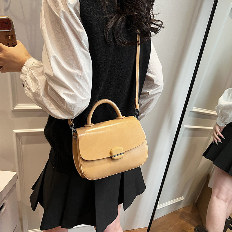 Beige crossbody handbag with flap front, oval buckle, curved handle, and crossbody strap