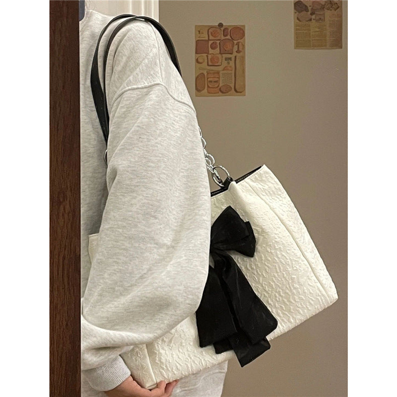 White canvas shoulder tote with black bow detail and silver chain strap