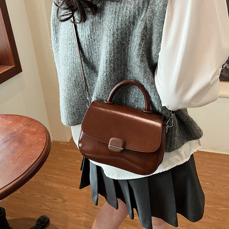 Brown crossbody handbag with flap closure and curved top handle