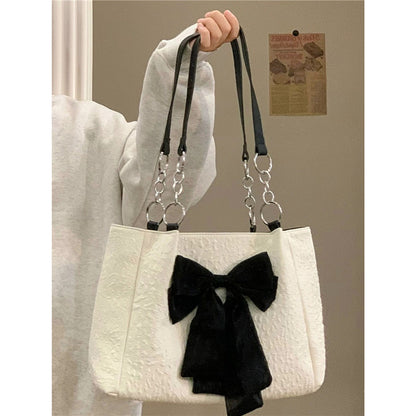 White canvas tote bag with black bow front and long chain shoulder straps
