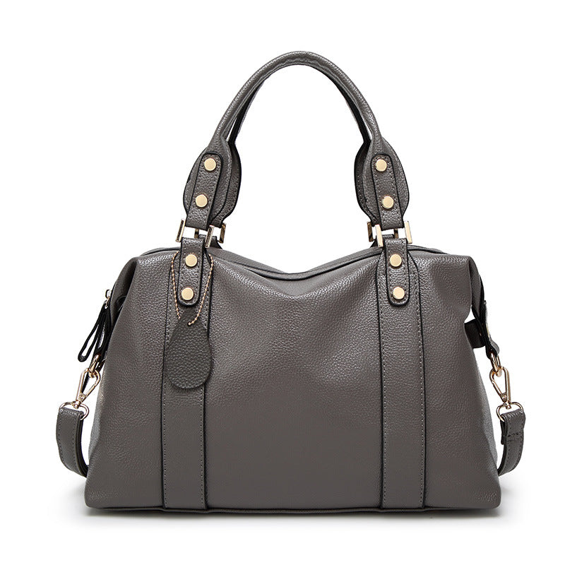 Grey shoulder bag with dual top handles, gold-stud strap tabs, and side tassel pulls
