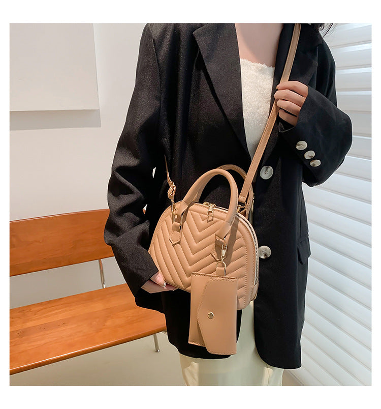 Beige quilted women's shoulder messenger bag with top handle, strap, and charm tag