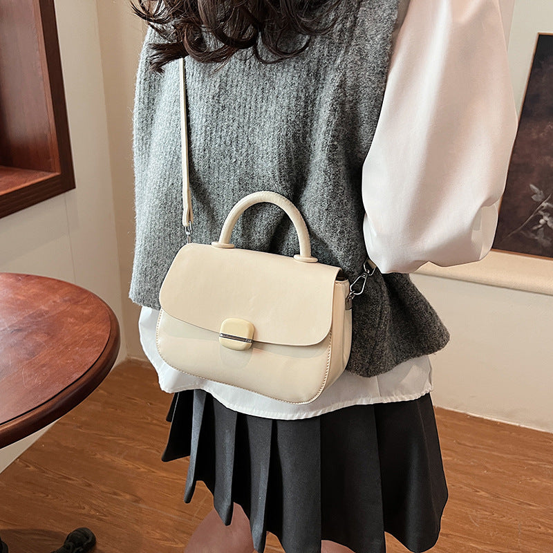 Off-white crossbody handbag with flap closure, gold-tone buckle, and short top handle