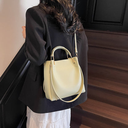 Light yellow bucket bag with curved handles and adjustable crossbody strap