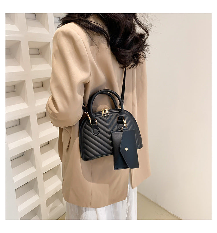 Black quilted women's shoulder messenger bag on model with top handle and charm tag