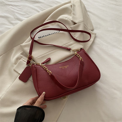 Red pebbled shoulder crossbody bag with gold chain strap, curved flap, and side tassel