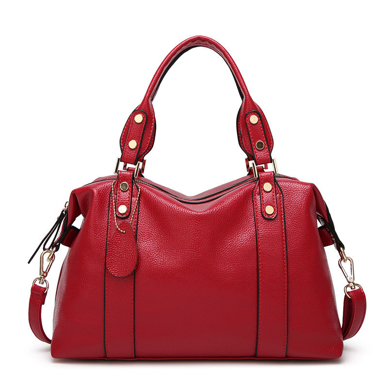 Red leather shoulder bag with dual handles, studded strap tabs, and side tassel pulls